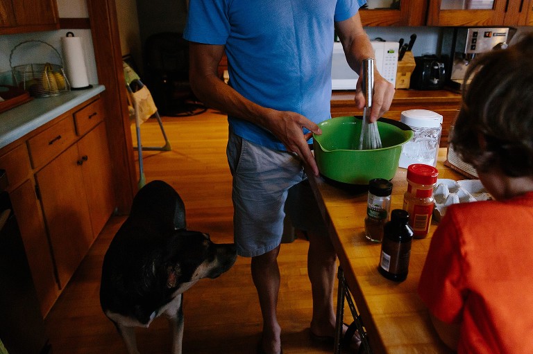 Dad whisks eggs in a green bowl while dog looks on.