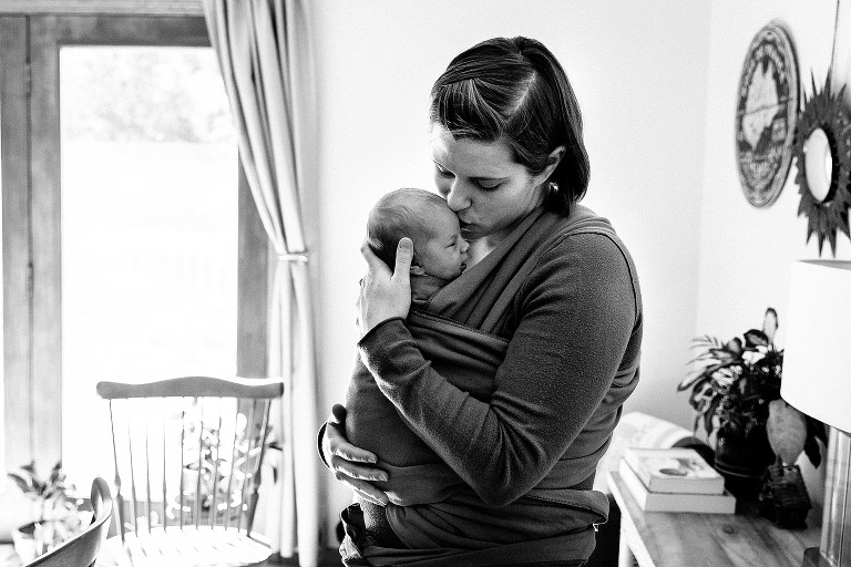 mom wears baby and kisses baby's head during madison newborn photo session