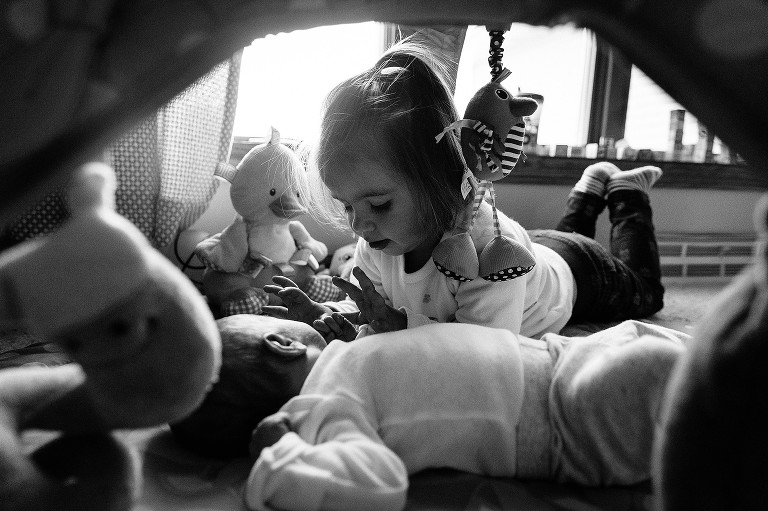Big sister plays with newborn sister's hands on a playmate.  Four