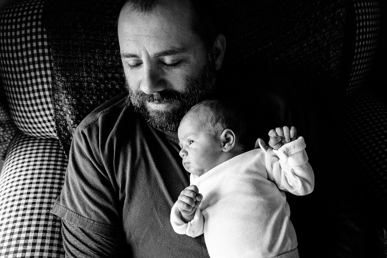 black and white. Dad holds newborn baby in soft window light, four