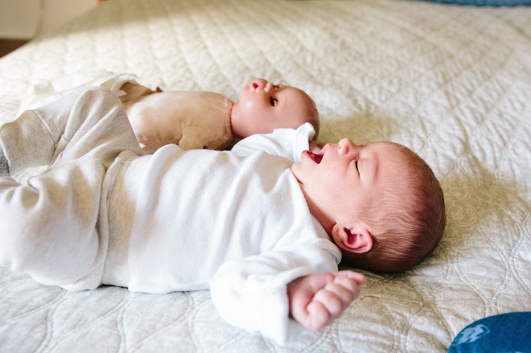 newborn baby on the bed with similar profile as big sister's doll lying beside her, four