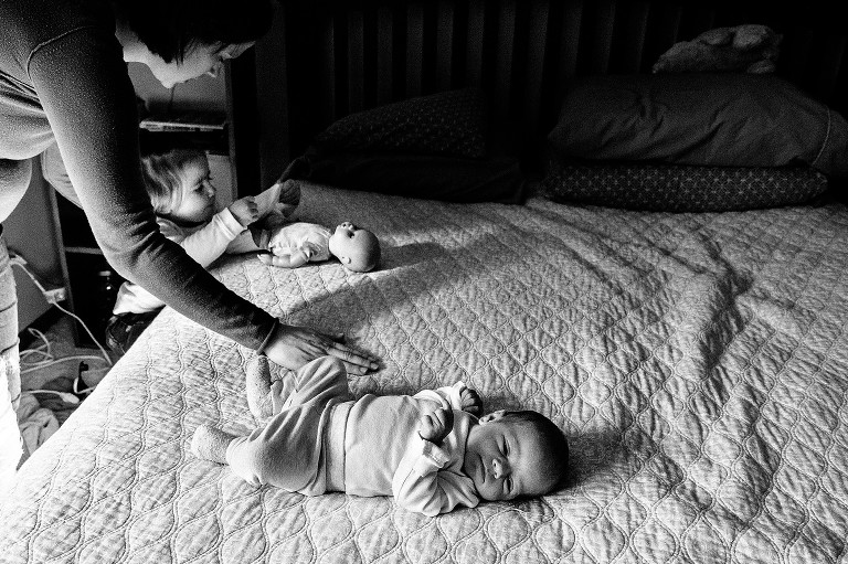 newborn on the bed while sister puts diaper on a her doll, becomes family of four