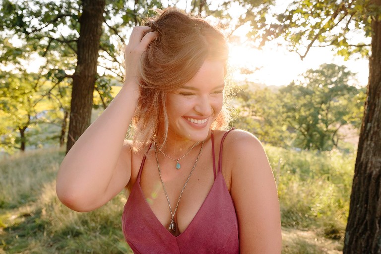 Young woman smiles in grassy forest at sunset