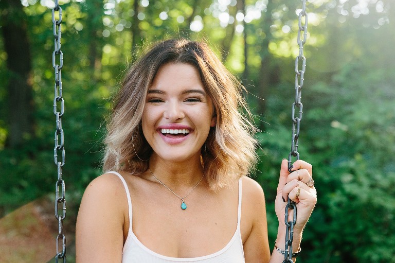 Young woman laughs while on swingset in the forest