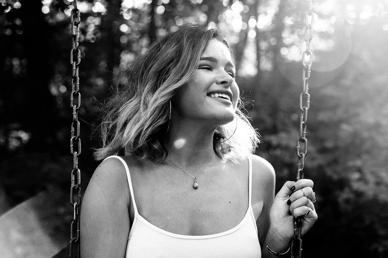 Black and white photo of young woman smiling on swingset