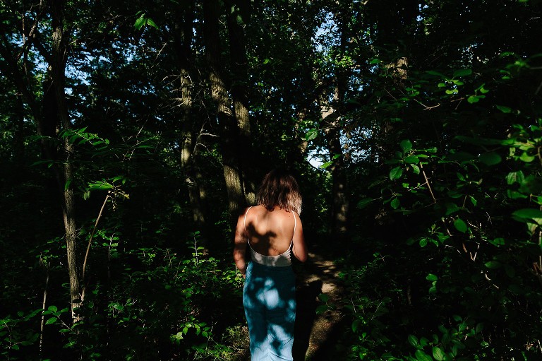 Young woman walks down wooded path.