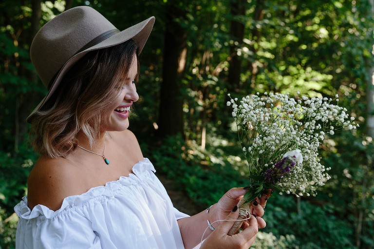 Young woman smiles at flowers in the forest.