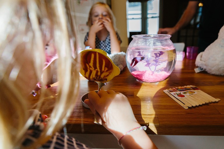 Girl scrapes chocolate batter into pan while sister watches from across the table 