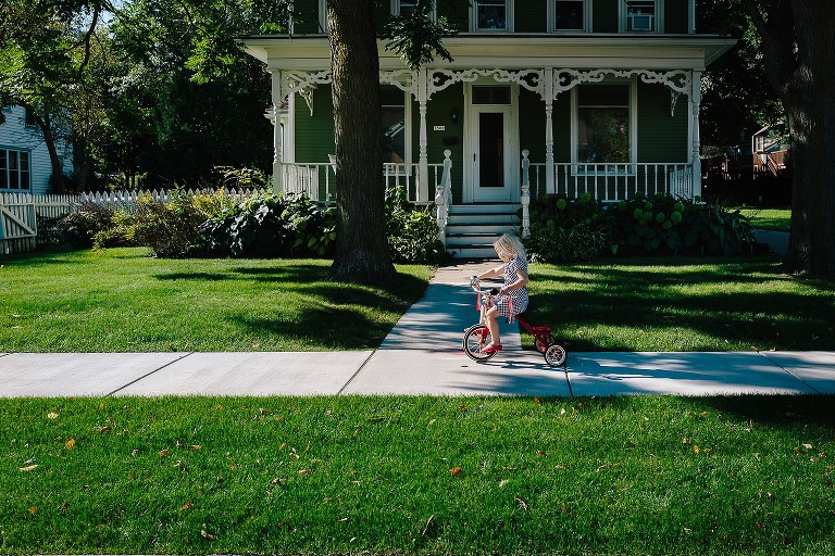 Girl rides tricycle in front of house 