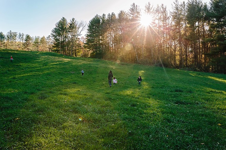 mom and four children walk up a hill, sunshine comes through the trees. 