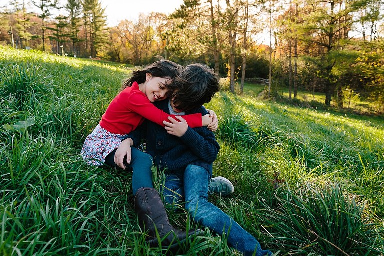 Brother and sister hug in the wind on a hill. 