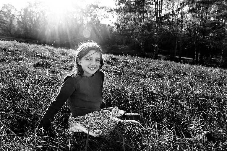 Daughter sits on a hill in the sun.