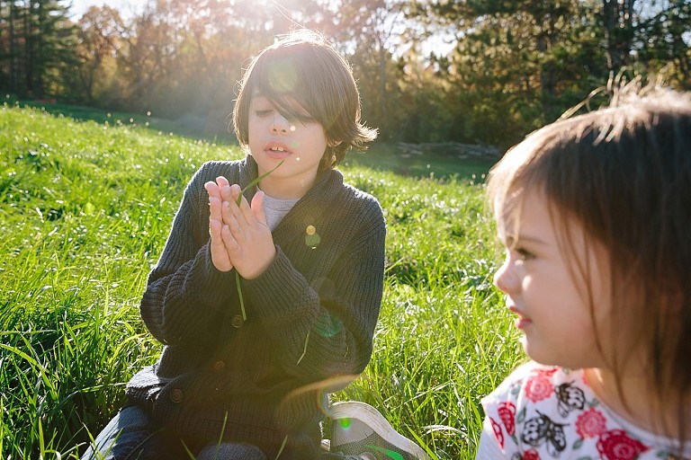 Son rolls blade of grass in hands. Sun flare in picture 