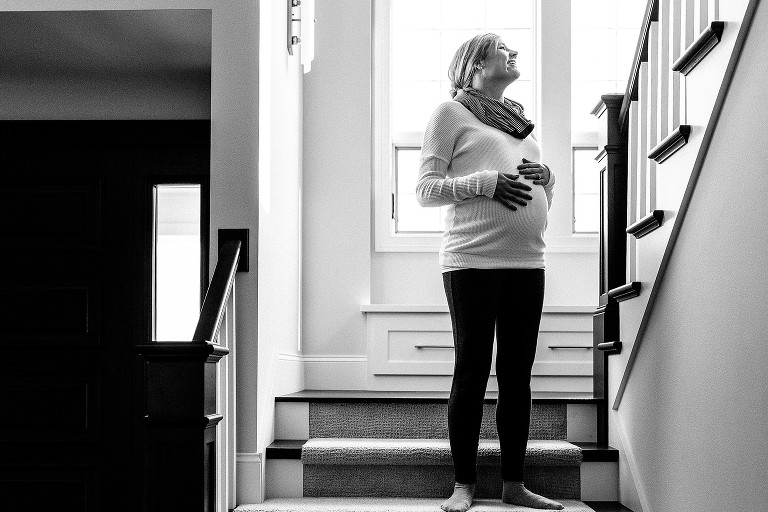 Black and white. Pregnant mother standing on stairwell looking up the stairs