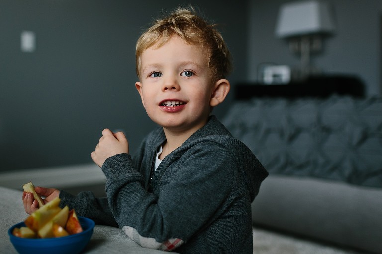 Young boy smiles while snacking on apple slices.