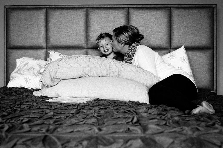 Black and white. Mother kisses son's cheek sitting on big bed together