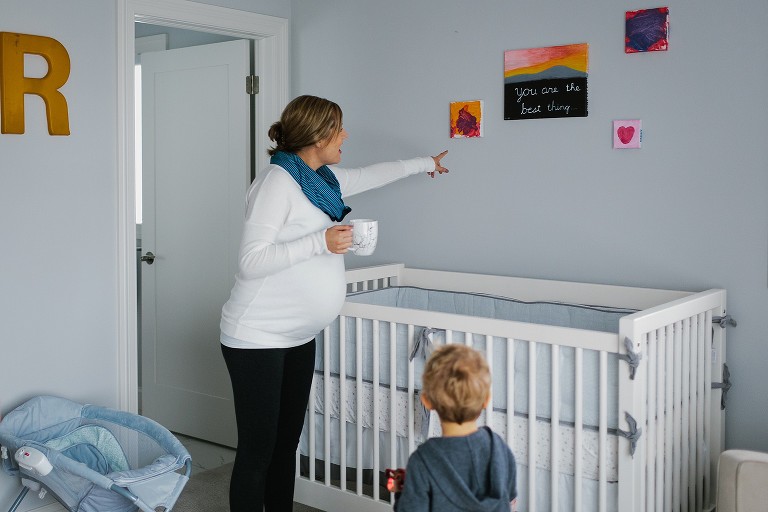 Mother showing baby's nursery with art on the walls to big brother