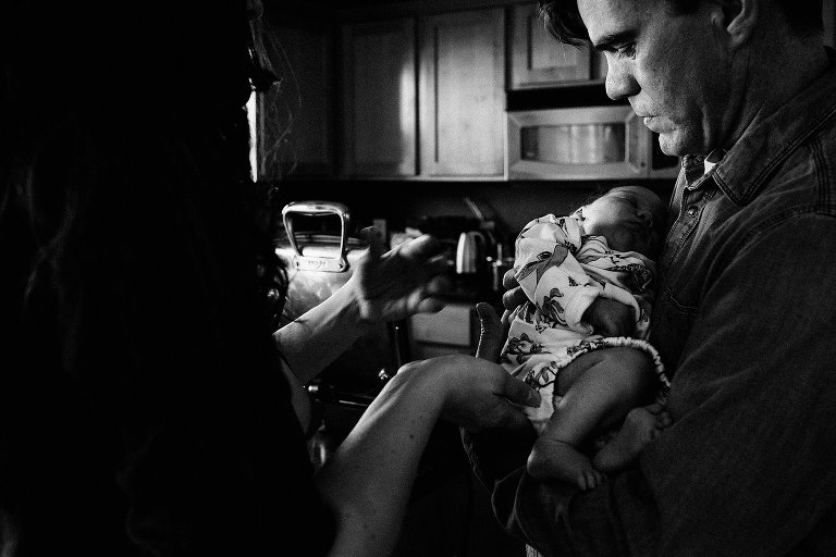 Mom hands off baby to Dad in kitchen 