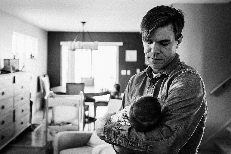 Dad looks at newborn daughter, son plays in the background 