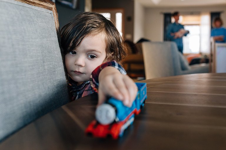 preschooler plays with Thomas the Train, Dad and Grandma in background 