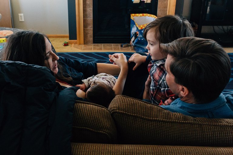 Mother nurses newborn and talks preschool boy and husband 