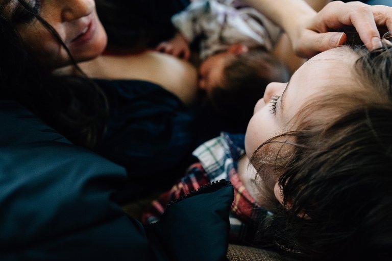Mother nurses newborn and holds preschool boy