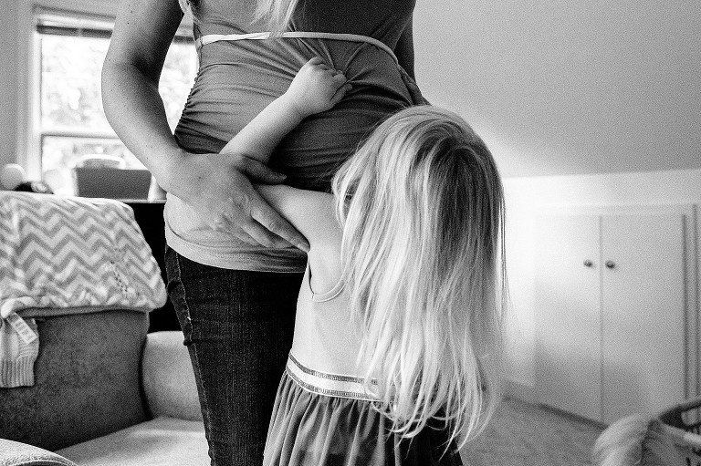 Daughter pulls on mom's shirt over pregnant belly 