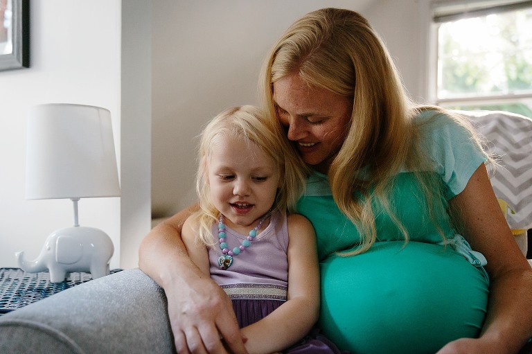 Pregnant mom and preschool daughter snuggle on a chair together