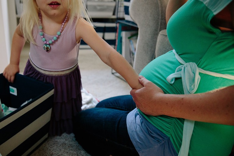 Pregnant mom holds daughter's hand over pregnant belly