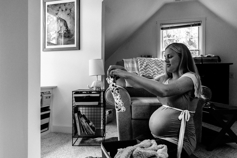 Black and white. Mom inspects newborn clothes, puts on folded pile 