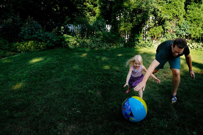 dad and preschool daughter both reach for big beach ball rolling away from them. 