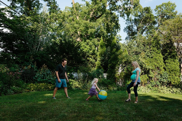 Family of three, dad, preschool girl, pregnant mom, kick a beach ball to each other in the backyard 