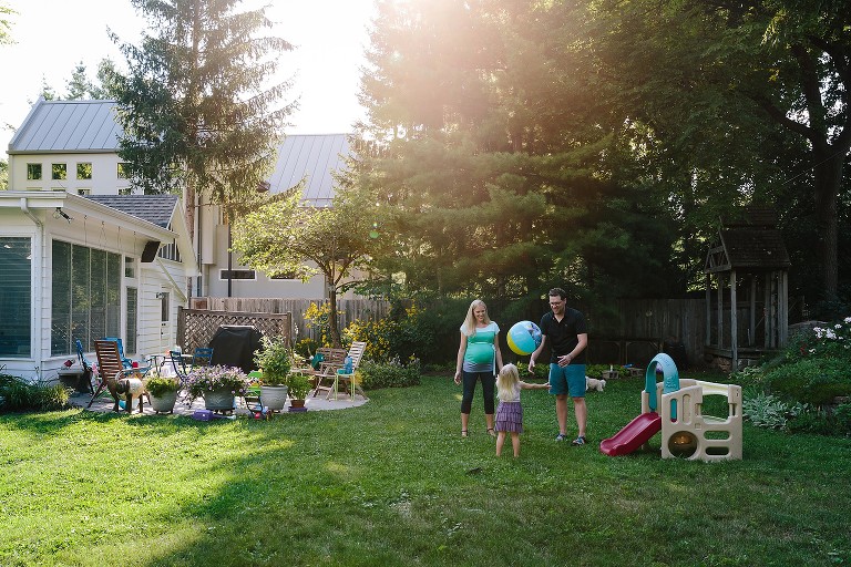 Family of three: Pregnant mom, dad, preschool girl toss a beach ball to each other in the backyard. 