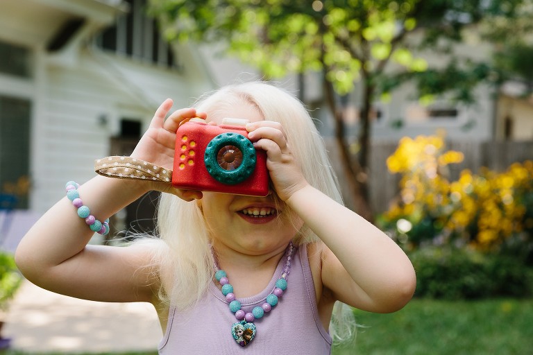 Preschool girl takes a pretend photo with toy camera