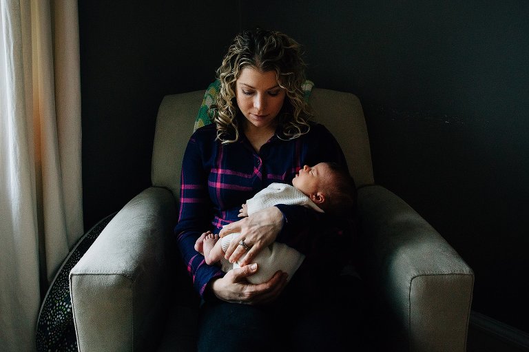 Mother sits in a chair with newborn daughter. 