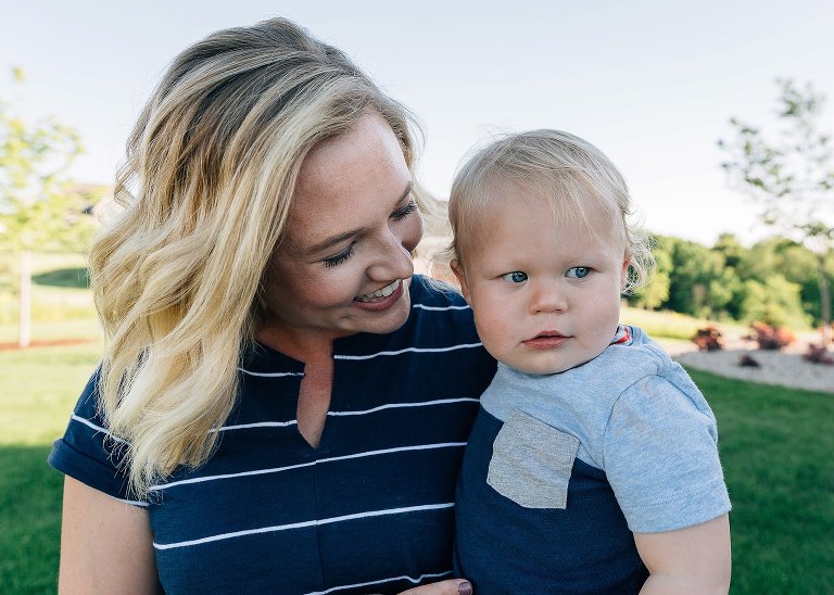 Mother holds toddler son, smiles at him, as the wind blows her hair. 