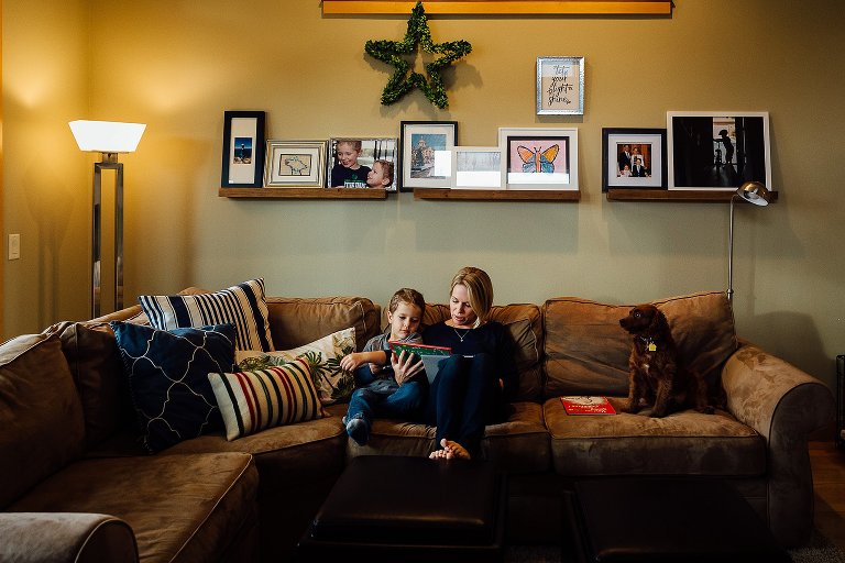 Mother sits on a couch and reads Christmas stories with her young son. 