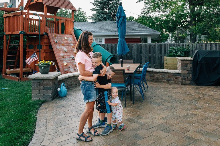Three children run to their mother in their backyard. 