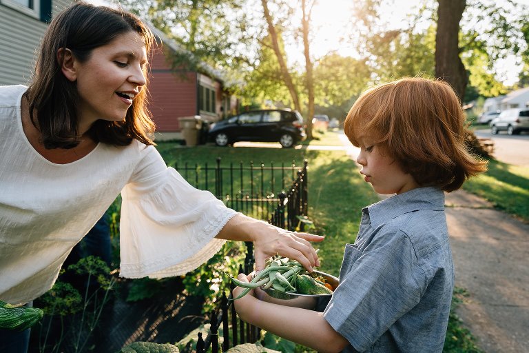 Mother drops a handful of garden beans into a bowl her son is holding for her. 