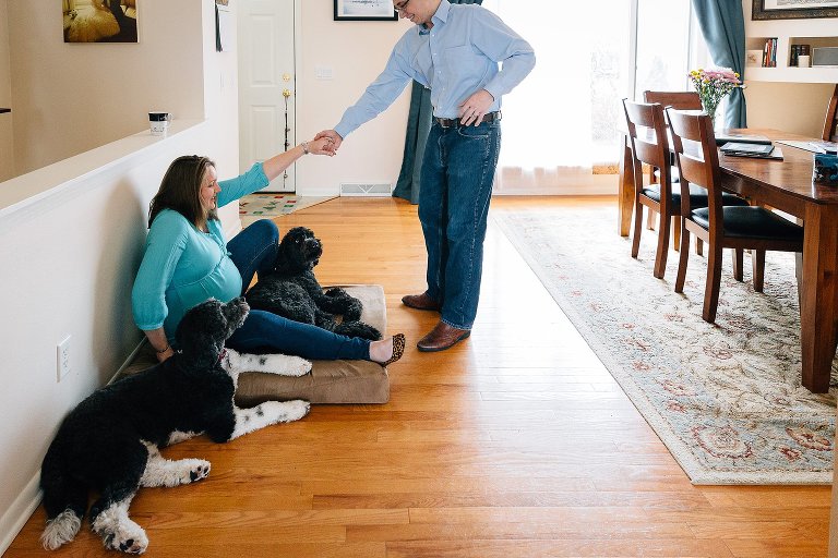 Father helps expectant mother up while two dogs lay at her side