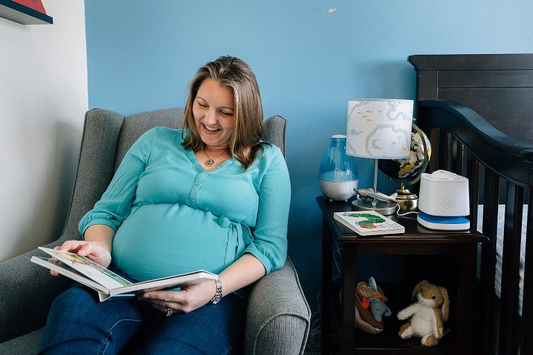 Expectant mother reads a board book in nursery chair 
