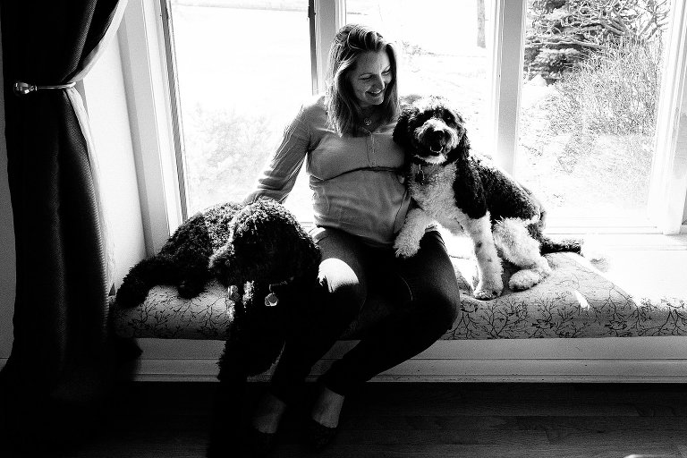 Expectant mother sits in sunny window with two family dogs 