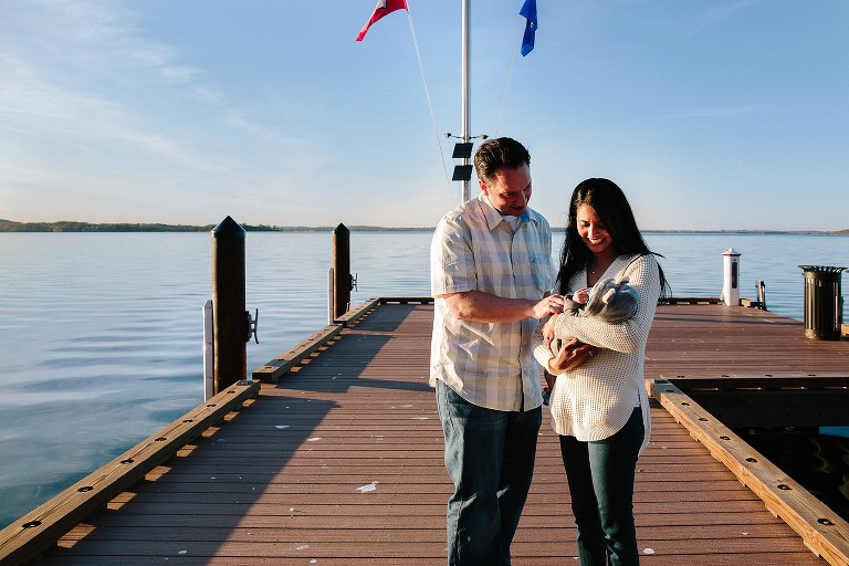 parents smile at newborn on hte lake pier 