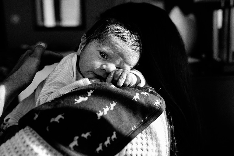 Mom burps newborn baby, baby has open eyes and eye contact with camera 
