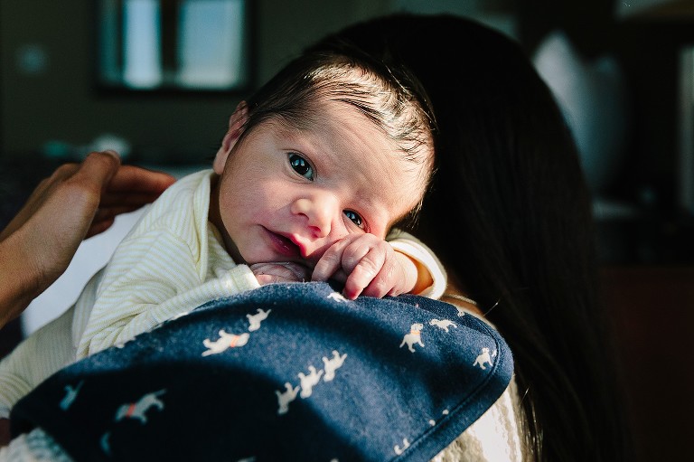 Mom burps newborn baby, baby has open eyes and eye contact with camera 