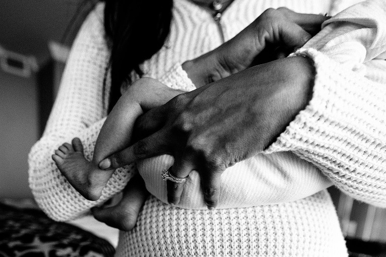 Detail shot of baby's feet adn mom's hands and wedding ring 