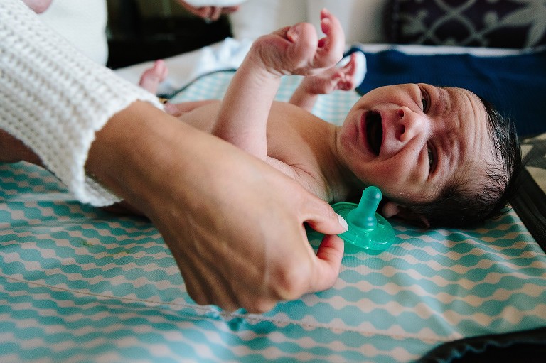 newborn baby cries as mom reaches for pacifier 