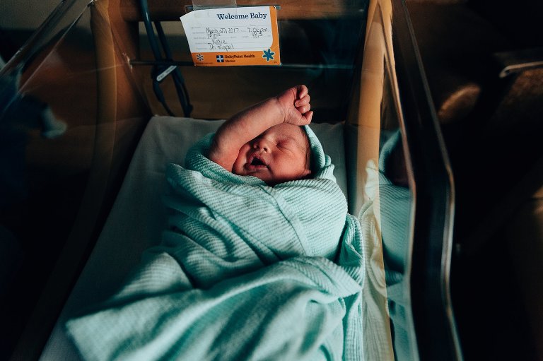 Baby covers eye with arm in hospital bassinet 