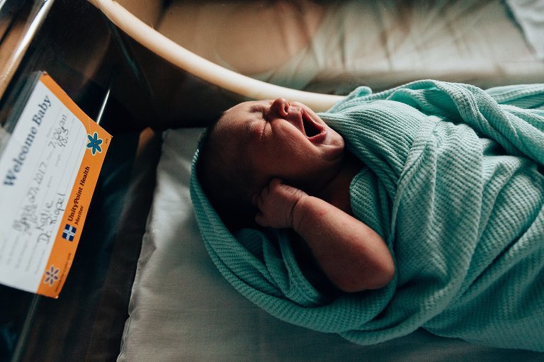 Baby yawns in hospital bassinet with birth details 