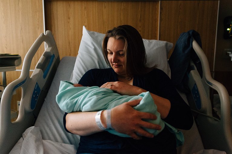 Mom looks at newborn baby in hospital bed. 